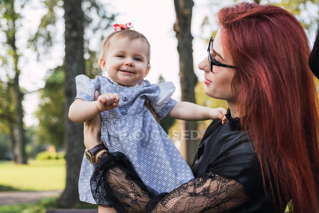 Donna che tiene in braccio la bambina eccitata nel parco — Foto stock