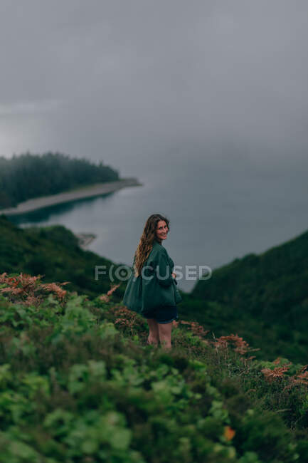 Женщина, стоящая на высоком холме с озером внизу — стоковое фото
