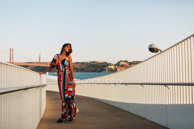 Elegante donna in abito lungo passeggiando sul ponte in città estiva — Foto stock