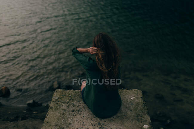 Jovem mulher sentada no penhasco perto do lago — Fotografia de Stock