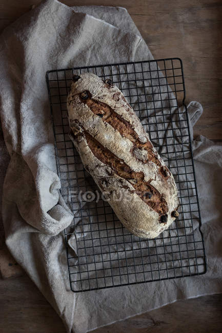 Loaf of delicious rye bread with cranberries and walnuts on grating on wooden tabletop — Stock Photo