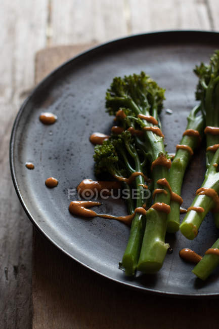 Gros plan de brocoli cuit à la vapeur avec sauce romesco sur une assiette noire sur une table en bois — Photo de stock