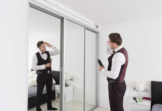 Seitenansicht eines jungen gutaussehenden Mannes in Hose und Weste, der im Schlafzimmer steht und in den Spiegel schaut — Stockfoto