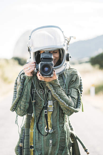 Girl wearing old space helmet and spacesuit taking photo with camera outdoors — Stock Photo