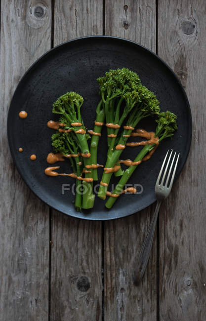 Brócolis cozido no vapor com molho romesco na placa preta com garfo na mesa de madeira — Fotografia de Stock