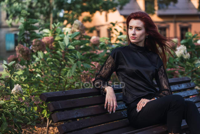 Retrato de elegante joven sentada en el banco en el parque - foto de stock