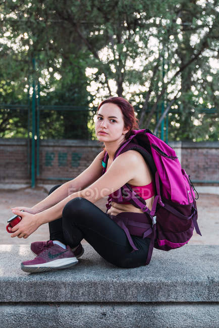 Portrait of young sportswoman with backpack sitting on stone with mug — Stock Photo