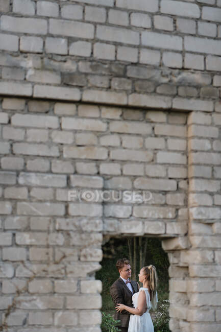 Newlywed man and woman embracing while standing at abandoned building — Stock Photo