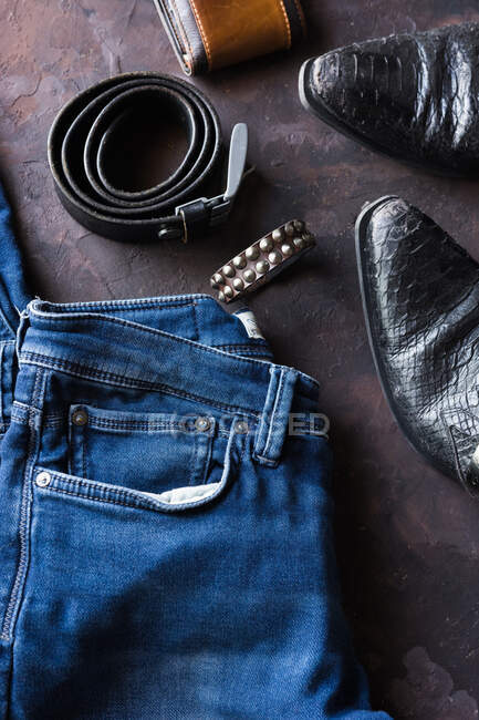 Vista aérea de ropa de mezclilla para hombre con billetera, brazalete de tachuelas, teléfono inteligente. y zapatos de cuero negro - foto de stock