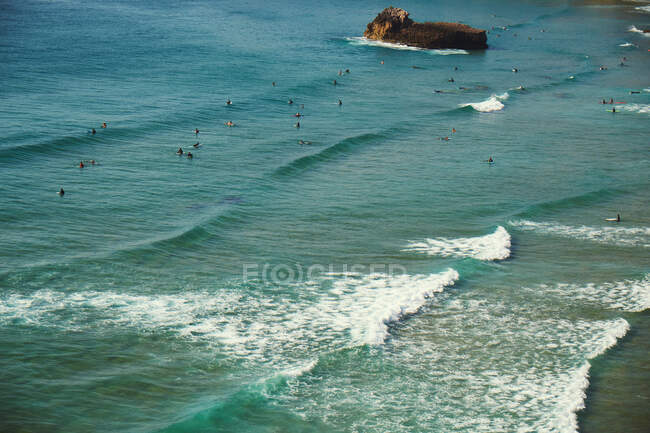 From above view of beach with many unrecognizable people and wavy clear water with rock daytime — Stock Photo