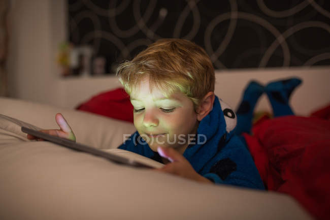 Sourire petit garçon regarder des dessins animés avec tablette numérique au lit — Photo de stock
