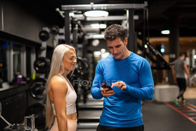 Atlético hombre y mujer usando teléfono inteligente en el gimnasio - foto de stock