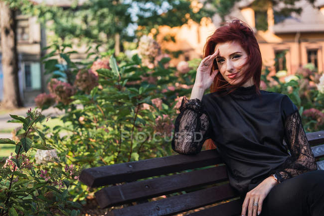 Retrato de elegante jovem sorridente senhora sentado no banco no parque — Fotografia de Stock