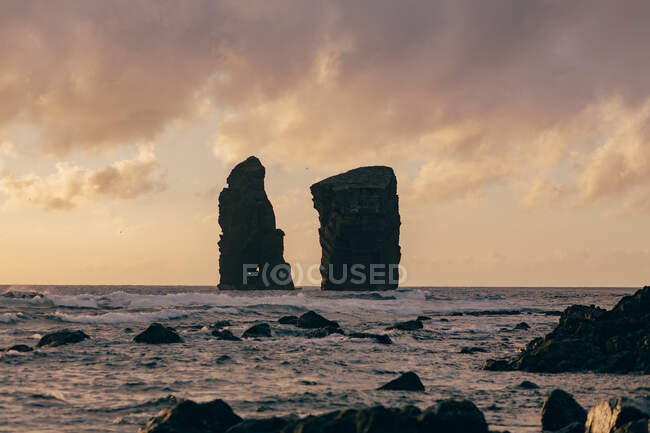 Высокие камни помещены в середине бурного моря на фоне неба, полного облаков — стоковое фото