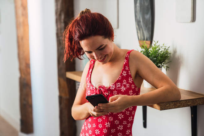 Jovem mulher usando smartphone e sorrindo em casa — Fotografia de Stock