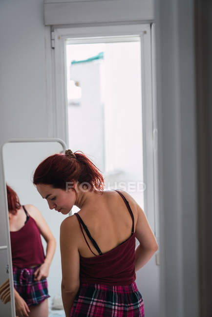 Вдумчивая молодая женщина стоит перед зеркалом — стоковое фото