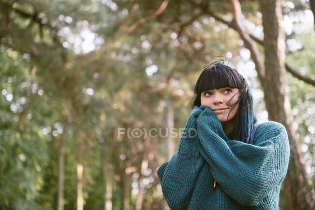 Дивовижна мрія брюнетка в сірому светрі стоїть в зеленому парку, дивлячись подалі — стокове фото