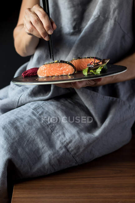 Woman talking delicious salmon fillets with chopsticks — Stock Photo