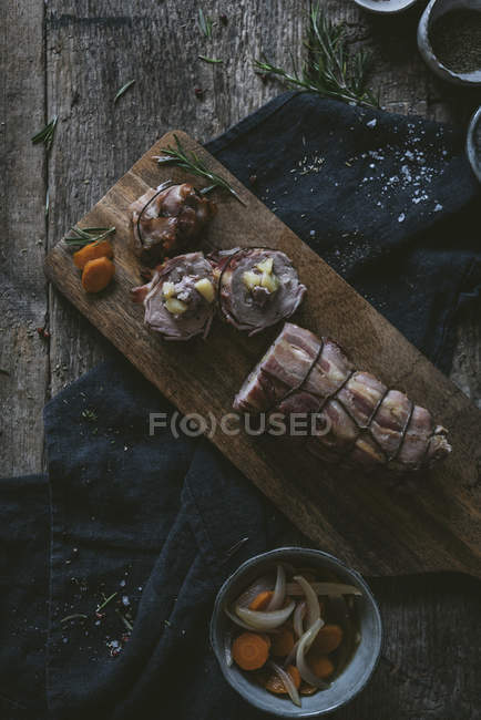 Solomillo de cerdo relleno sobre mesa de madera con especias e ingredientes - foto de stock