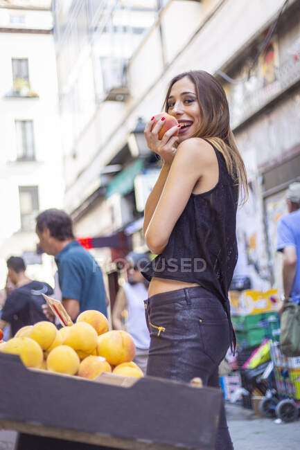 Веселая женщина кусает персик на рынке — стоковое фото