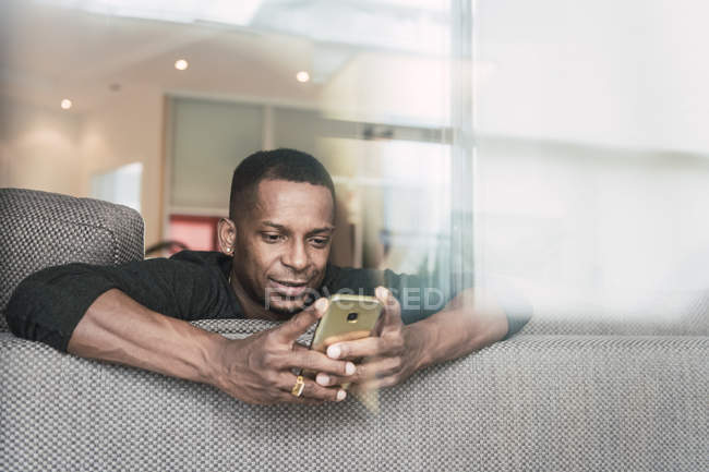 African American man using smartphone on sofa at home — Stock Photo