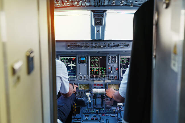 Panel de control de cabina con visualizadores e indicadores y dos pilotos en uniforme navegando en un avión - foto de stock