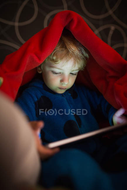 Маленький мальчик в пижаме с цифровым планшетом под одеялом — стоковое фото