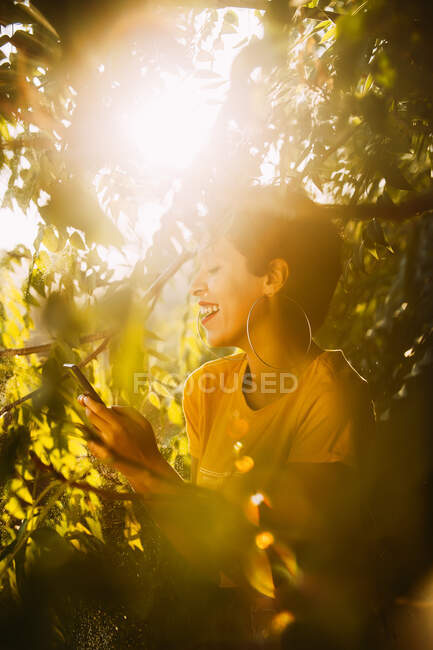 Vista lateral de la atractiva joven hembra con smartphone en el jardín - foto de stock