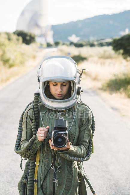 Girl wearing old space helmet and spacesuit holding photo camera outdoors — Stock Photo