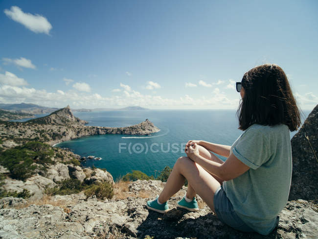 Mulher pensativa sentada na costa rochosa e olhando para a vista — Fotografia de Stock