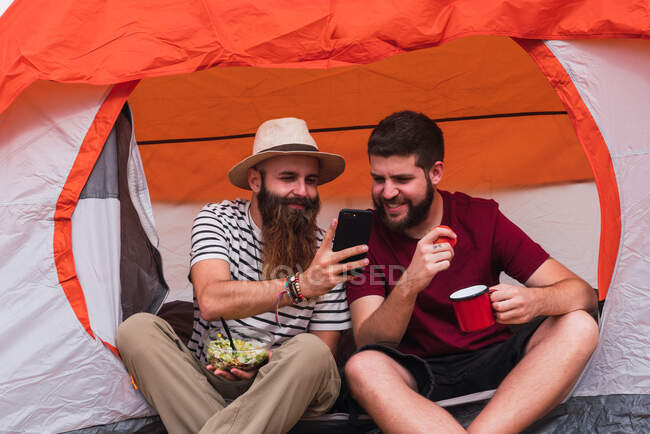 Viajantes comendo e perto da tenda com smartphone — Fotografia de Stock