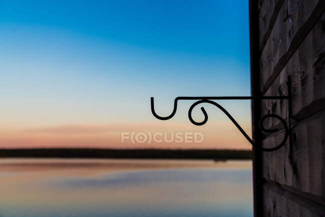 Black patterned hook on stone wall on background of blue still lake and cloudless sky — Stock Photo