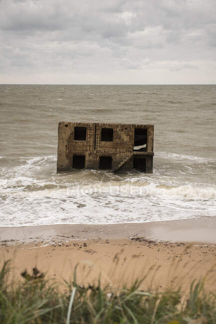Exterior of aged abandoned house in water with waves of ocean running on beach — Stock Photo
