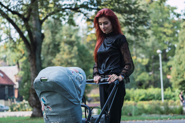 Jeune femme élégante marchant avec poussette bébé dans le parc — Photo de stock