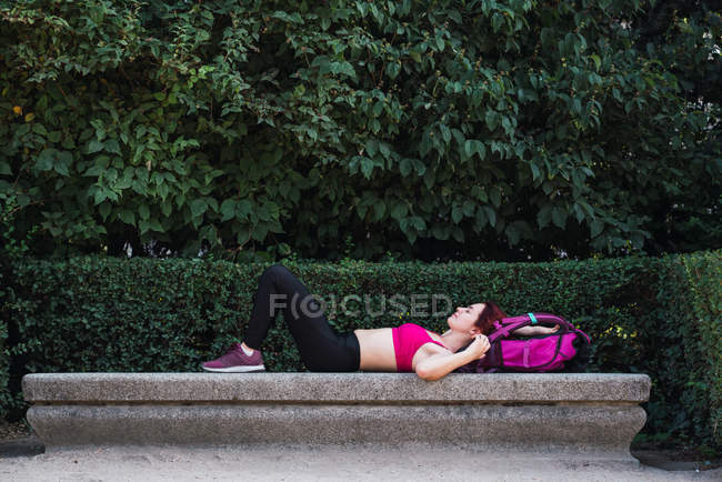 Sportiva sdraiata su panchina in pietra nel parco con zaino — Foto stock