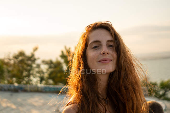 Attrayant jeune femme souriant et regardant la caméra tout en se tenant debout sur un fond flou de nature étonnante par une journée ensoleillée en Bulgarie, Balkans — Photo de stock