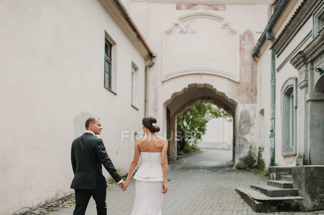 Вид ззаду молодого чоловіка і нареченого тримає руки під час прогулянки на красивій вулиці старого міста — стокове фото