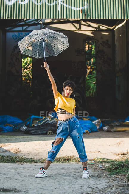 Portrait of young woman in stylish outfit posing with transparent umbrella on sunny day — Stock Photo