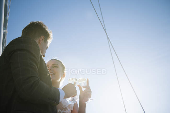 Newlywed man and woman clinking glasses of champagne on background of clear sky in sunny day — Stock Photo