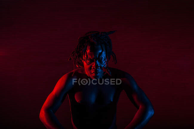 Young african rastafarian man enjoys rehearsing and plays tam tam, colored lighting red and blue — Stock Photo