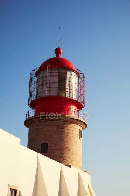 Dipinto in cima rossa di faro e fondo da mattoni su edificio bianco su sfondo con cielo azzurro chiaro — Foto stock