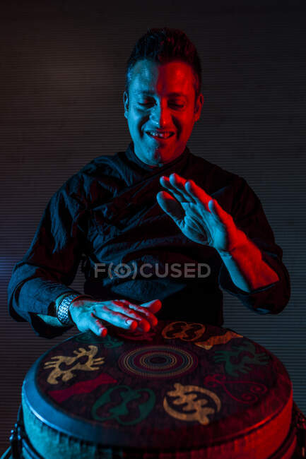 Young percussionist practicing technique with the tam tam or drum, colored lighting in red and blue. — Stock Photo