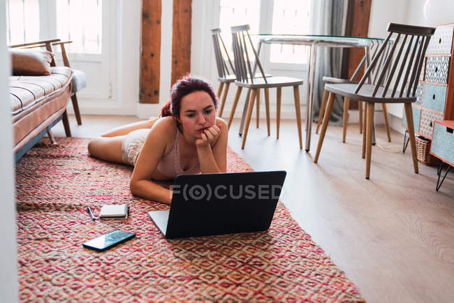 Jovem deitada no chão em casa e usando laptop — Fotografia de Stock