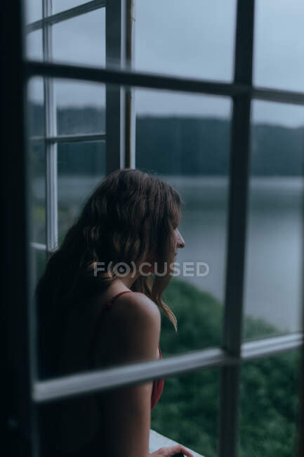 Femme regardant par la fenêtre de la chambre — Photo de stock