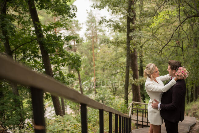 Dall'alto colpo di abbracciare gli sposi adulti in piedi su passerella di legno in boschi verdi — Foto stock