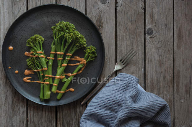 Broccoli al vapore con salsa romesco su piatto nero con forchetta su tavolo di legno — Foto stock