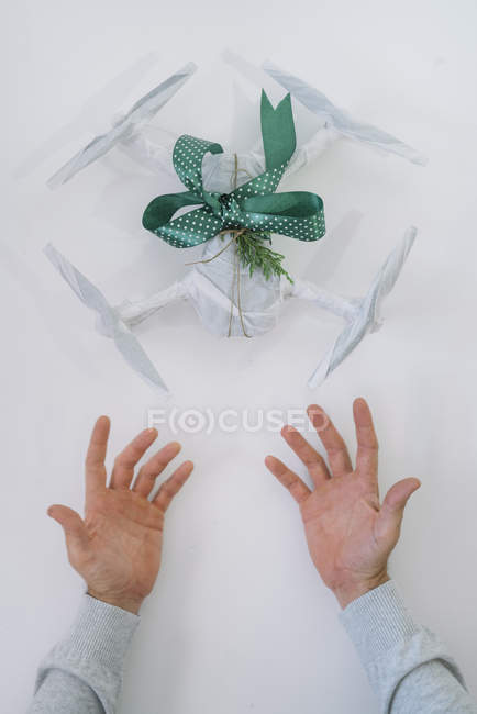 Чоловічі руки з загорнутим дроном як різдвяний подарунок з ялиновою гілкою та зеленою стрічкою на білому тлі — стокове фото
