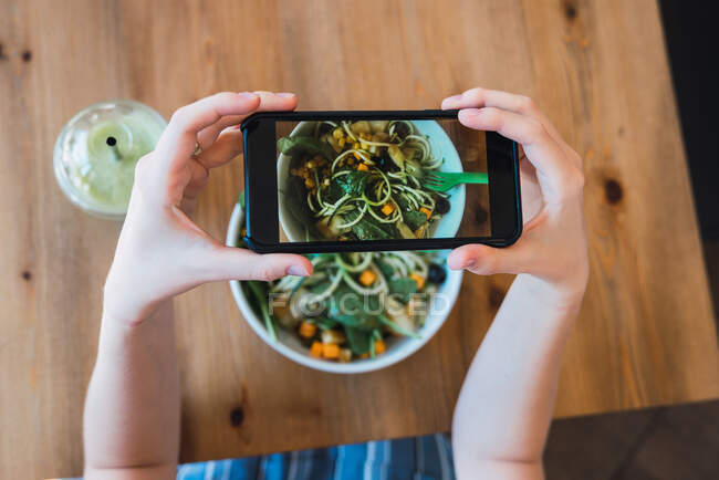 Colpo di raccolto dall'alto di donna utilizzando smartphone e scattando foto di insalata sul tavolo — Foto stock