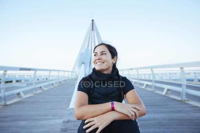 Femme en sportswear noir debout sur la construction moderne du pont regardant confiant — Photo de stock