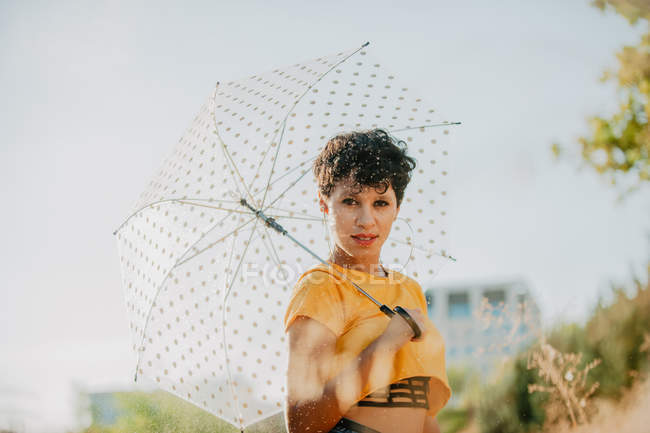 Portrait of young woman with umbrella standing under drops of spraying water — Stock Photo